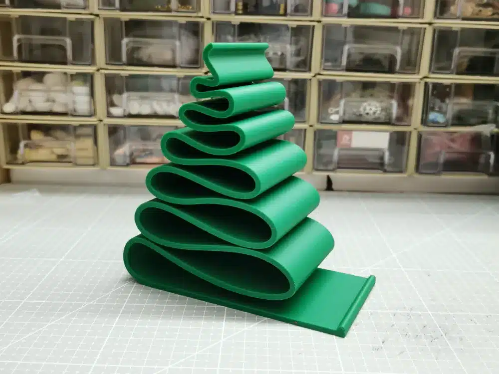 Green 3D printed wave sculpture on crafting table with organized drawers in the background.