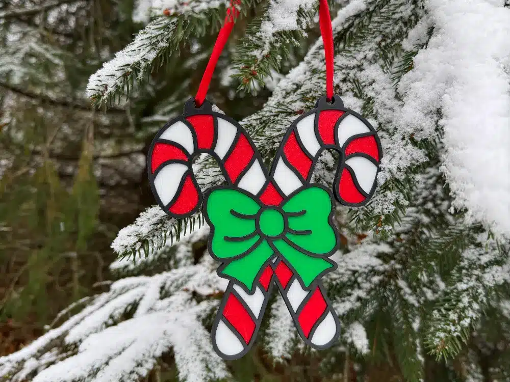 Festive candy cane ornament with green bow hanging on snowy pine tree branch, capturing holiday spirit outdoors.