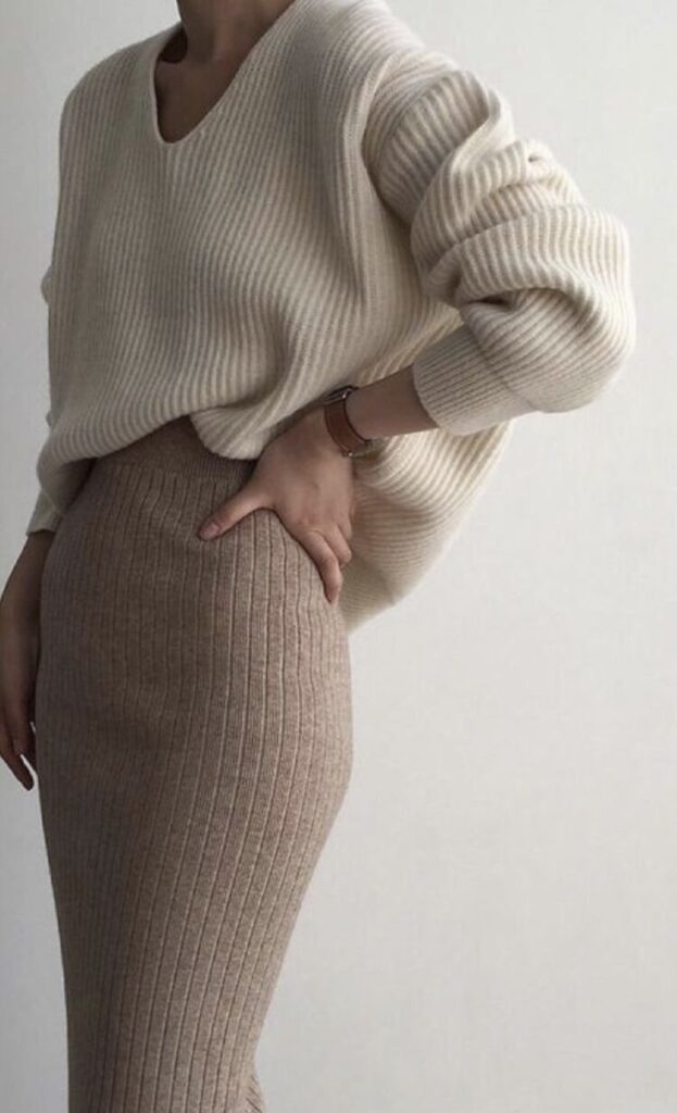 Cozy autumn fashion: woman in a beige ribbed sweater and skirt, posing stylishly against a minimalistic background.