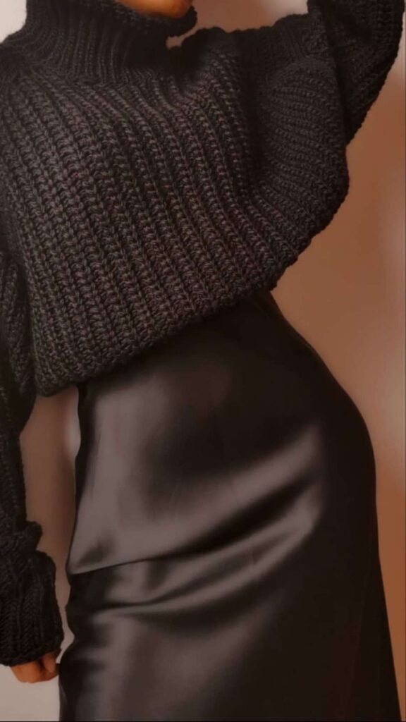 A person wearing a chunky black knit sweater paired with a sleek, black satin skirt, showcasing a stylish, modern fashion look.