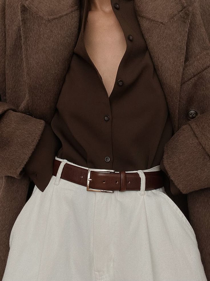 Stylish brown blouse, wool coat, and white pants with belt, perfect for a chic autumn look. Fashionable layered outfit close-up.