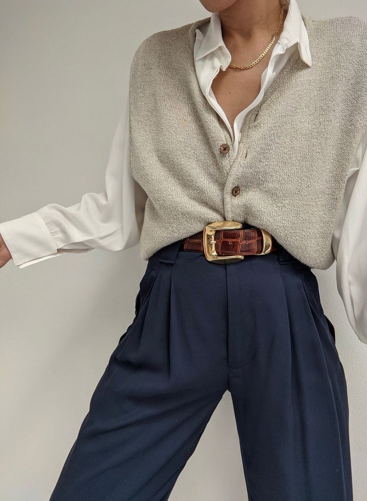 Fashionable outfit with a beige sweater vest, white shirt, pleated navy high-waist trousers, and a vintage brown belt with gold buckle.
