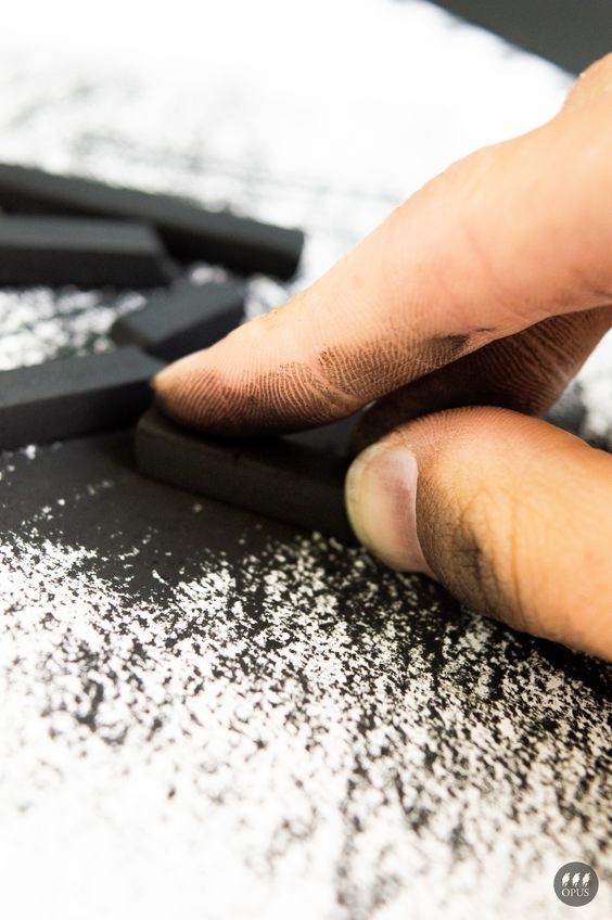 Close-up of a hand using black pastel chalk on textured paper, creating art with streaks and smudges for a creative drawing project.