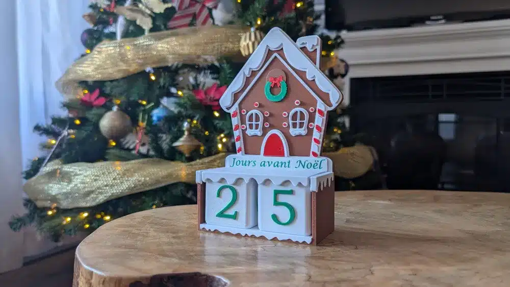 Gingerbread house countdown to Christmas with 25 days remaining, set against a decorated tree and festive home background.