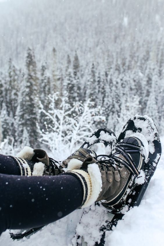 Snow-covered boots on a snowy mountain, surrounded by a dense forest in winter. Perfect for cold weather hiking adventures.