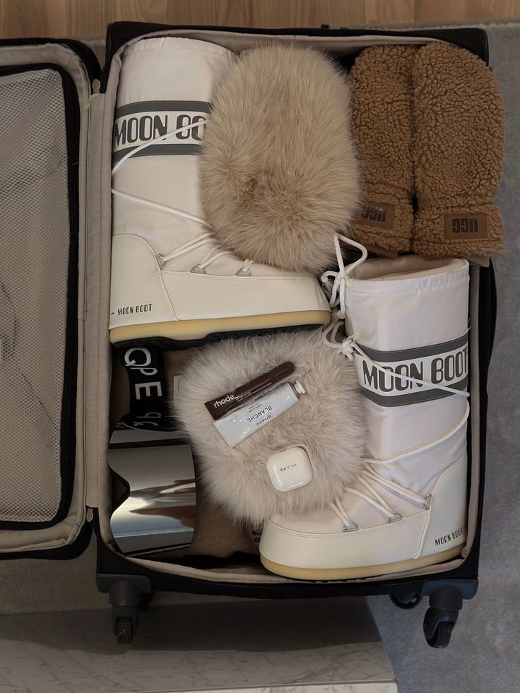 Open suitcase with white snow boots, furry mittens, and brown slippers, ready for a cozy winter getaway.