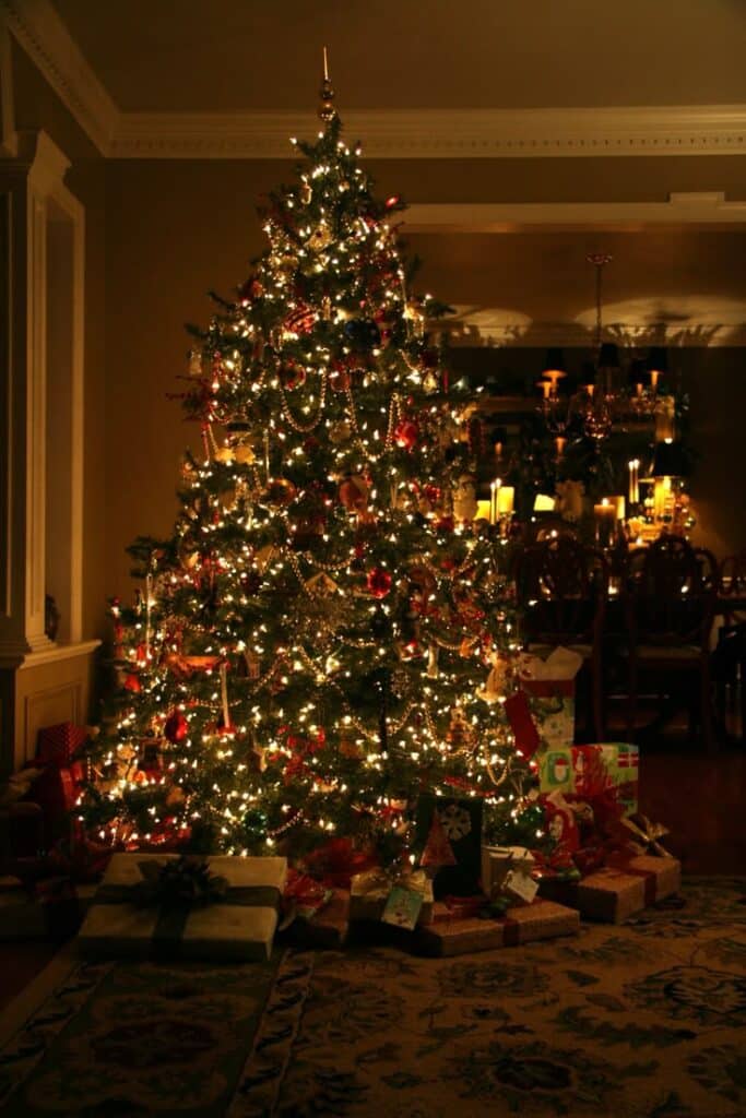 Beautifully decorated Christmas tree with lights and ornaments, surrounded by wrapped gifts in a cozy living room setting.