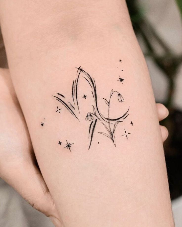 Minimalist botanical tattoo with flowers and stars on forearm, showcasing delicate black line art and nature-inspired design.