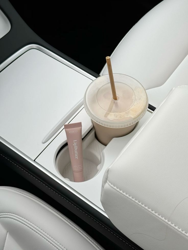 Car interior with lip balm and iced coffee in cup holders on white leather seats.