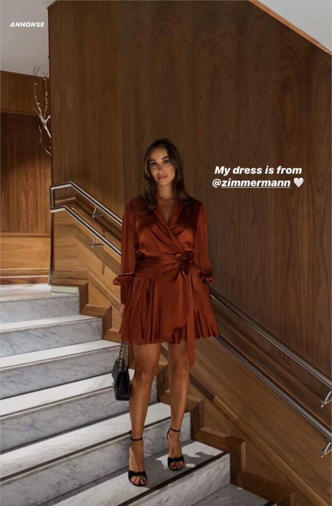 _ 23 Woman in chic rust-colored wrap dress posing on sleek staircase, holding a black bag. Dress from Zimmermann. | Sky Rye Design Woman in chic rust-colored wrap dress posing on sleek staircase, holding a black bag. Dress from Zimmermann.