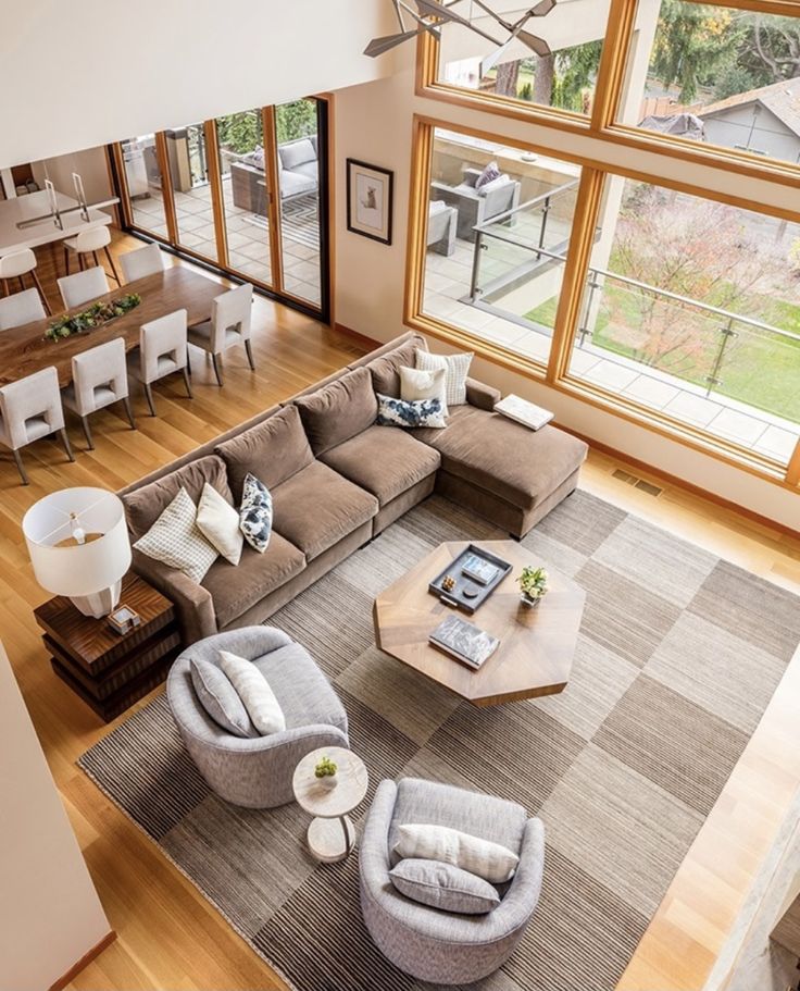 Screenshot Spacious modern living room with large windows, sectional sofa, armchairs, and wooden table overlooking a patio. | Sky Rye Design Spacious modern living room with large windows, sectional sofa, armchairs, and wooden table overlooking a patio.