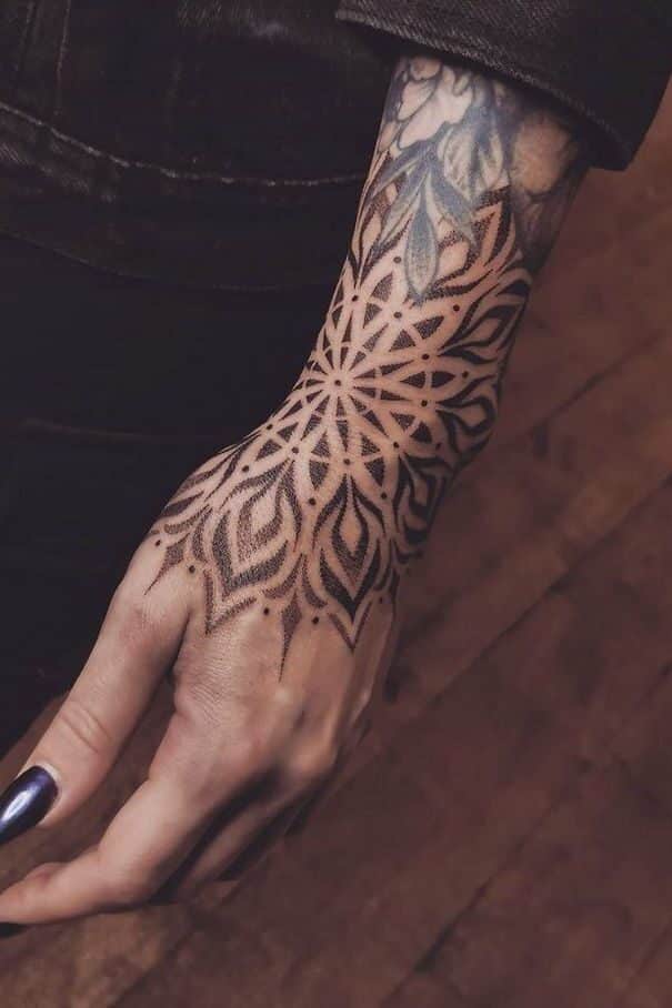 Close-up of a hand showcasing an intricate floral-patterned tattoo with dark nail polish, expressing artistic style. tattoos