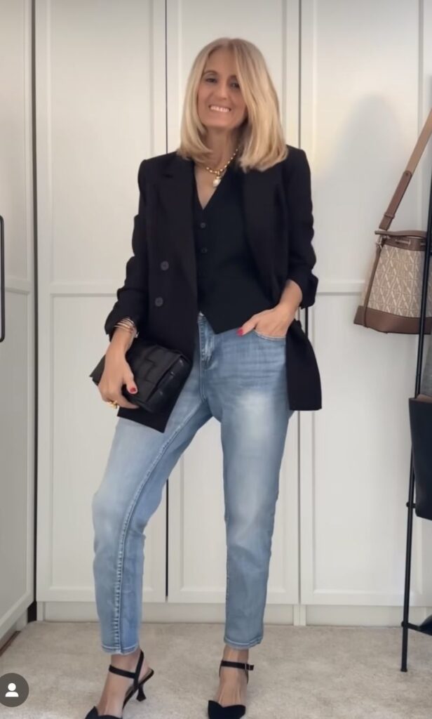 _ 25 Stylish woman in black blazer and jeans holds a clutch, showcasing a chic casual outfit in a modern room. Fashion and style inspiration. | Sky Rye Design Stylish woman in black blazer and jeans holds a clutch, showcasing a chic casual outfit in a modern room. Fashion and style inspiration.