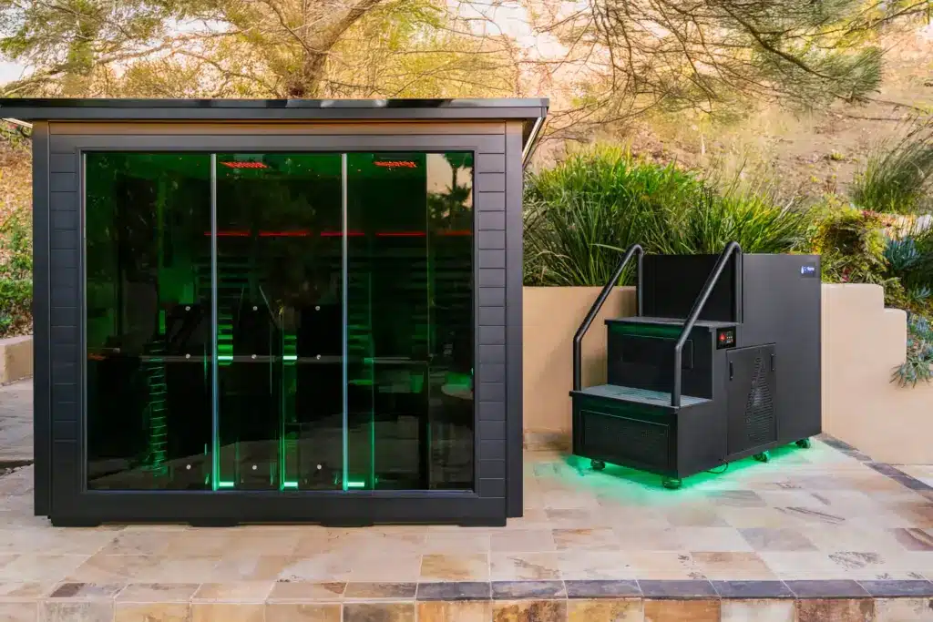 Infrared sauna with modern design and outdoor ice bath setup in a natural setting, featuring sleek black panels and ambient lighting.
