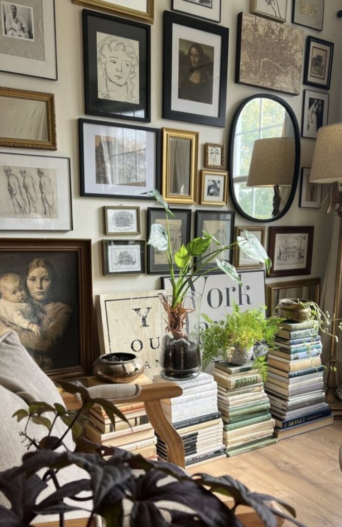Screenshot Gallery wall with various art frames, stacked books, and houseplants, creating a cozy and artistic living space. | Sky Rye Design Gallery wall with various art frames, stacked books, and houseplants, creating a cozy and artistic living space.
