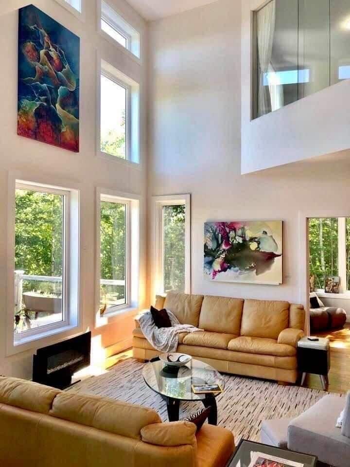 _ 26 Spacious modern living room with tall windows, tan sofas, colorful artwork, and a cozy ambiance. | Sky Rye Design Spacious modern living room with tall windows, tan sofas, colorful artwork, and a cozy ambiance.