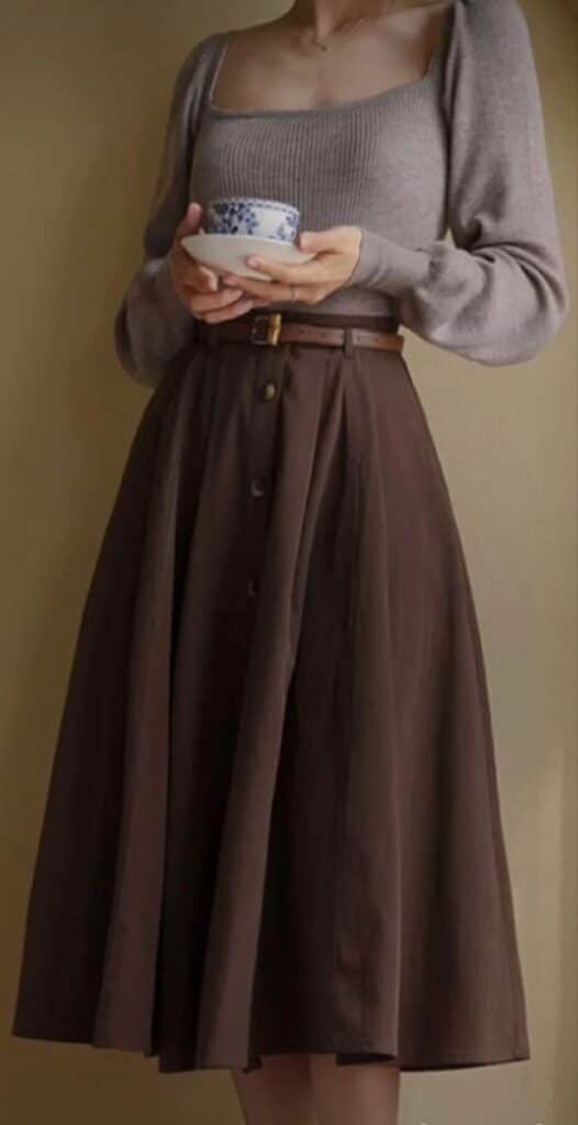 _ 27 Woman in a brown midi skirt and taupe sweater holds a blue and white teacup, highlighting a cozy, vintage-inspired fashion look. | Sky Rye Design Woman in a brown midi skirt and taupe sweater holds a blue and white teacup, highlighting a cozy, vintage-inspired fashion look.