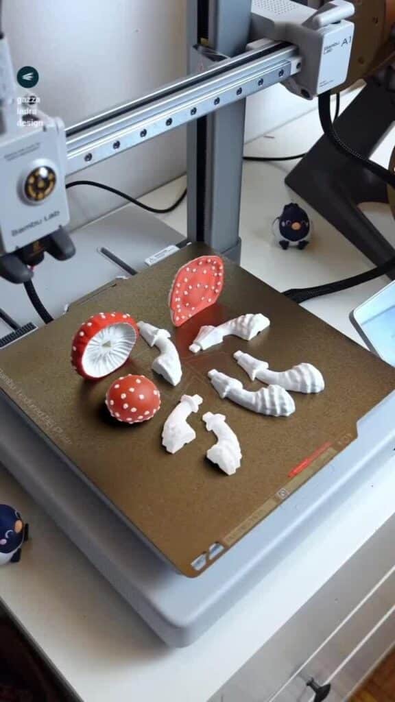 3D printer creating detailed red and white mushroom models with various components on the printing bed.
