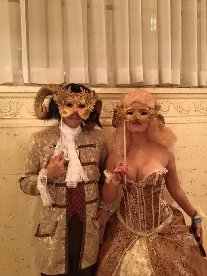 _ 29 Two people in elegant costumes and masks at a Venetian masquerade themed event, standing indoors. | Sky Rye Design Two people in elegant costumes and masks at a Venetian masquerade themed event, standing indoors.