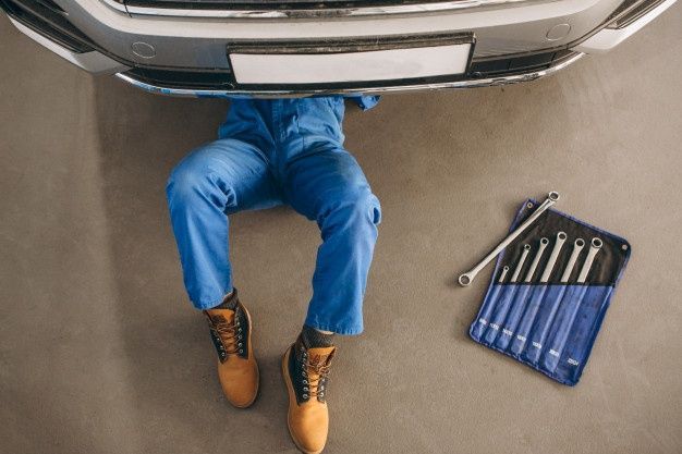 _ 3 Mechanic in blue coveralls working under a car with a set of wrenches nearby. | Sky Rye Design Mechanic in blue coveralls working under a car with a set of wrenches nearby.
