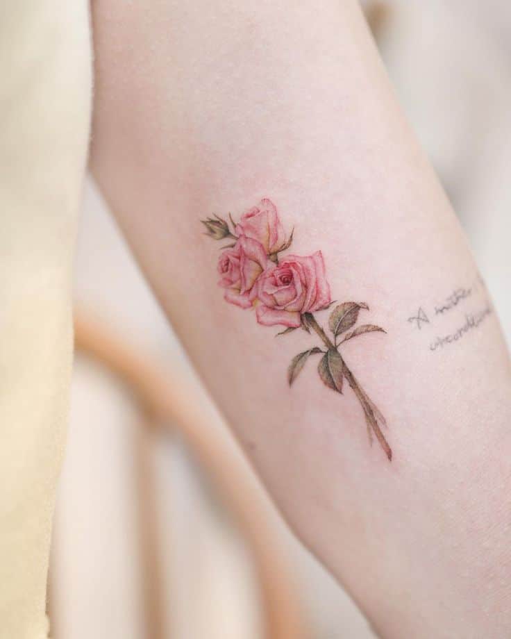 Pink rose tattoo on forearm with delicate script, symbolizing beauty and elegance.
