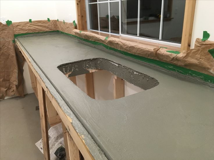 DIY concrete countertop project in progress, with fresh concrete curing in a kitchen setting featuring a hole for a sink installation.