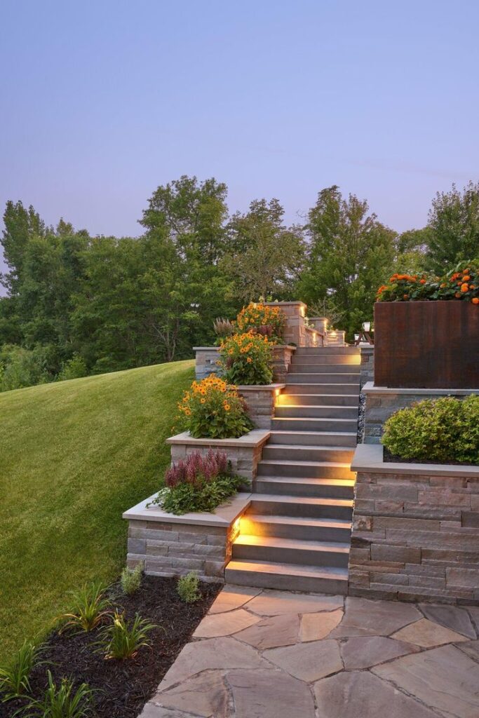 Illuminated stone garden steps adorned with colorful flowers against a twilight sky, surrounded by lush greenery.