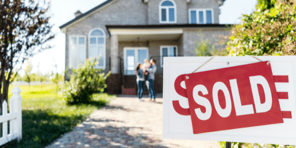 House with a Sold sign in front and a family standing outside, symbolizing a real estate purchase.