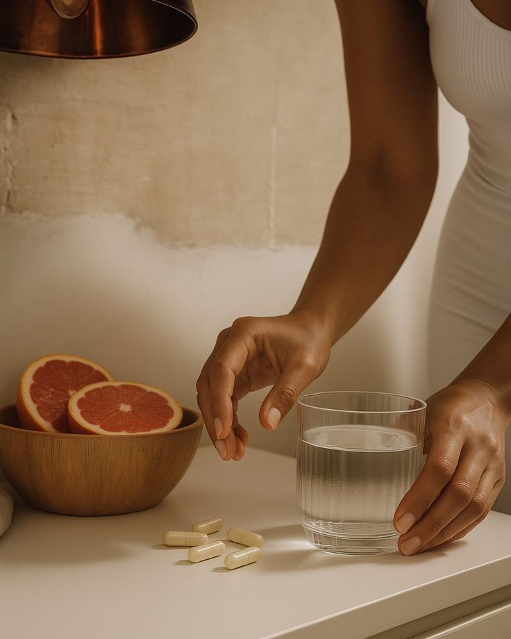 _ 30 Person holding a glass of water near vitamins and sliced grapefruit on a kitchen counter. | Sky Rye Design Person holding a glass of water near vitamins and sliced grapefruit on a kitchen counter.