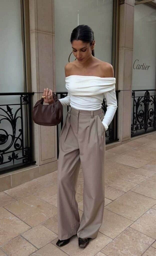 _ 30 Stylish woman in an off-shoulder white top and beige wide-leg pants, holding a brown purse, with a boutique backdrop. | Sky Rye Design Stylish woman in an off-shoulder white top and beige wide-leg pants, holding a brown purse, with a boutique backdrop.