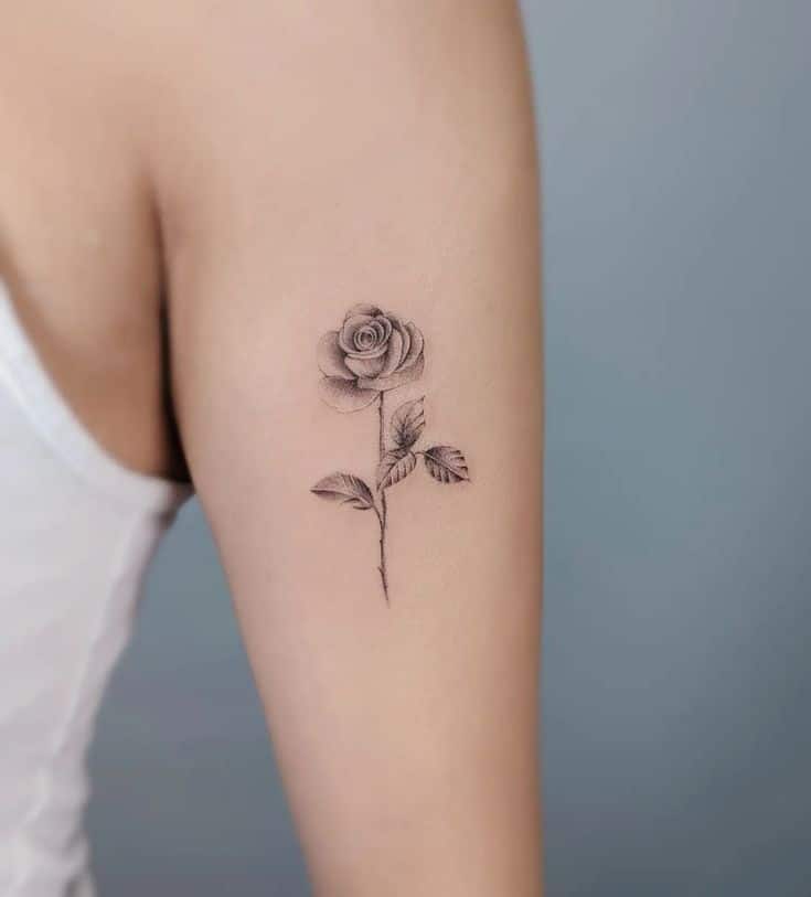 Minimalist rose tattoo on upper arm showcasing delicate shading and intricate details against a neutral background.