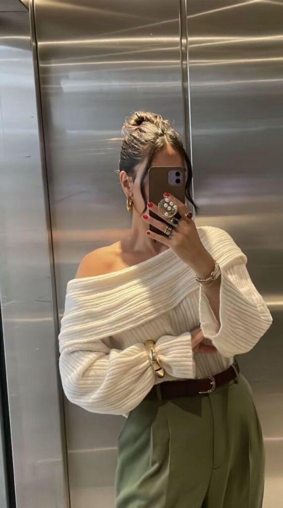 Screenshot Stylish woman in off-shoulder sweater and green pants takes a mirror selfie in an elevator, showcasing chic fashion and accessories. | Sky Rye Design Stylish woman in off-shoulder sweater and green pants takes a mirror selfie in an elevator, showcasing chic fashion and accessories.