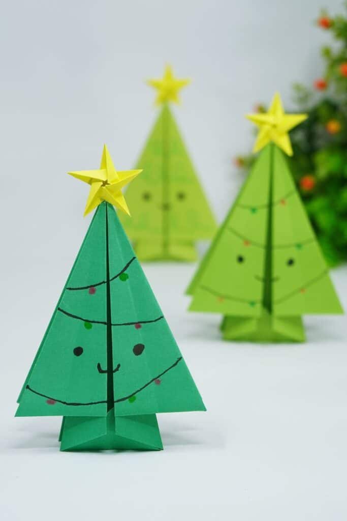 Cute origami Christmas trees with smiling faces and yellow star toppers, perfect for festive decorations and holiday crafts.