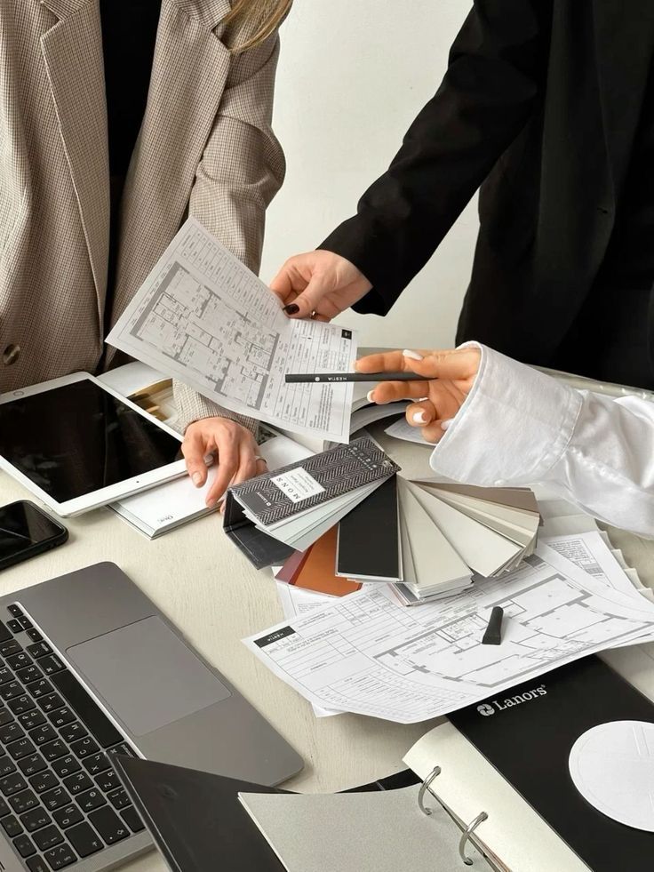 Architects discussing blueprints and material samples at a desk with a laptop, enhancing workspace design and collaboration.