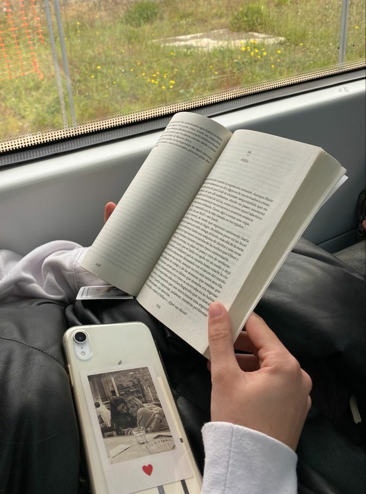 34840a5cb9734c02dc1aa919c99afe31 Person reading a book by a train window, with a phone nearby featuring a photo inside the case. | Sky Rye Design Person reading a book by a train window, with a phone nearby featuring a photo inside the case.