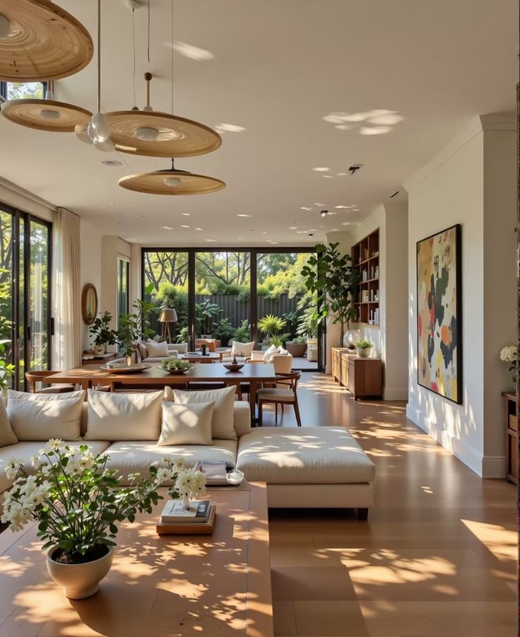 Spacious, sunlit living room with modern decor, wooden floors, cozy white sofas, and large windows overlooking a lush garden.