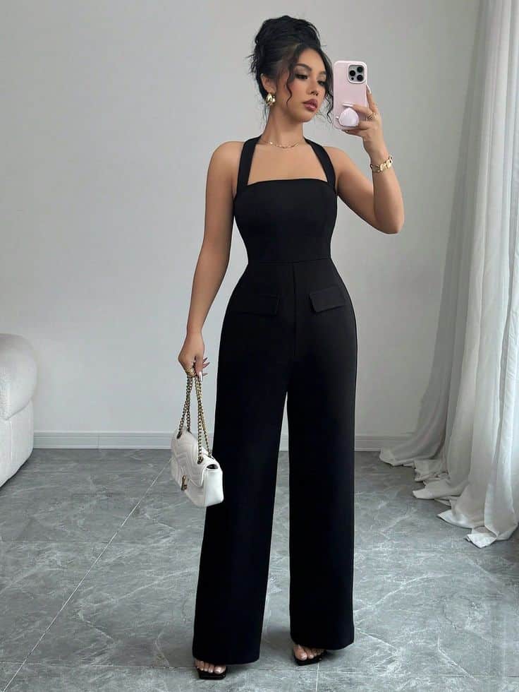 _ 37 Woman in elegant black jumpsuit takes a mirror selfie, accessorized with gold earrings, bracelet, and a white handbag in modern room. | Sky Rye Design Woman in elegant black jumpsuit takes a mirror selfie, accessorized with gold earrings, bracelet, and a white handbag in modern room.