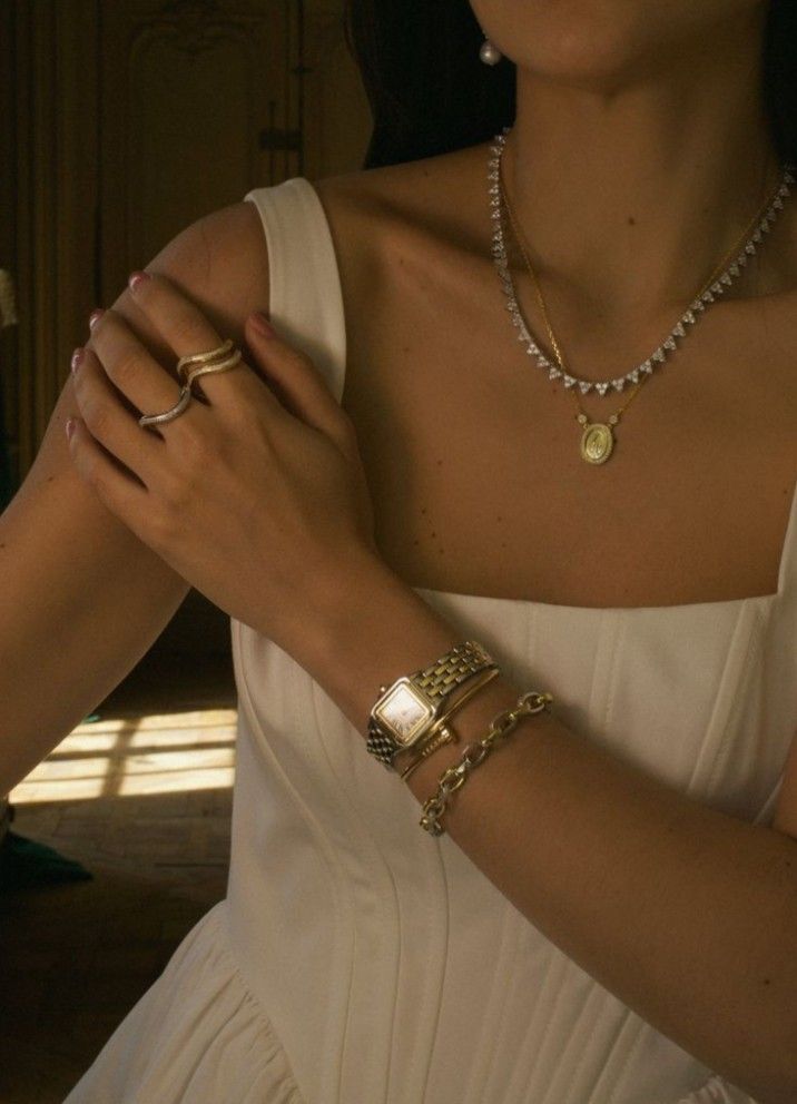 _ 38 Woman in elegant white dress wearing layered necklaces, gold watch, and rings, showcasing sophisticated style and fashion accessories. | Sky Rye Design Woman in elegant white dress wearing layered necklaces, gold watch, and rings, showcasing sophisticated style and fashion accessories.