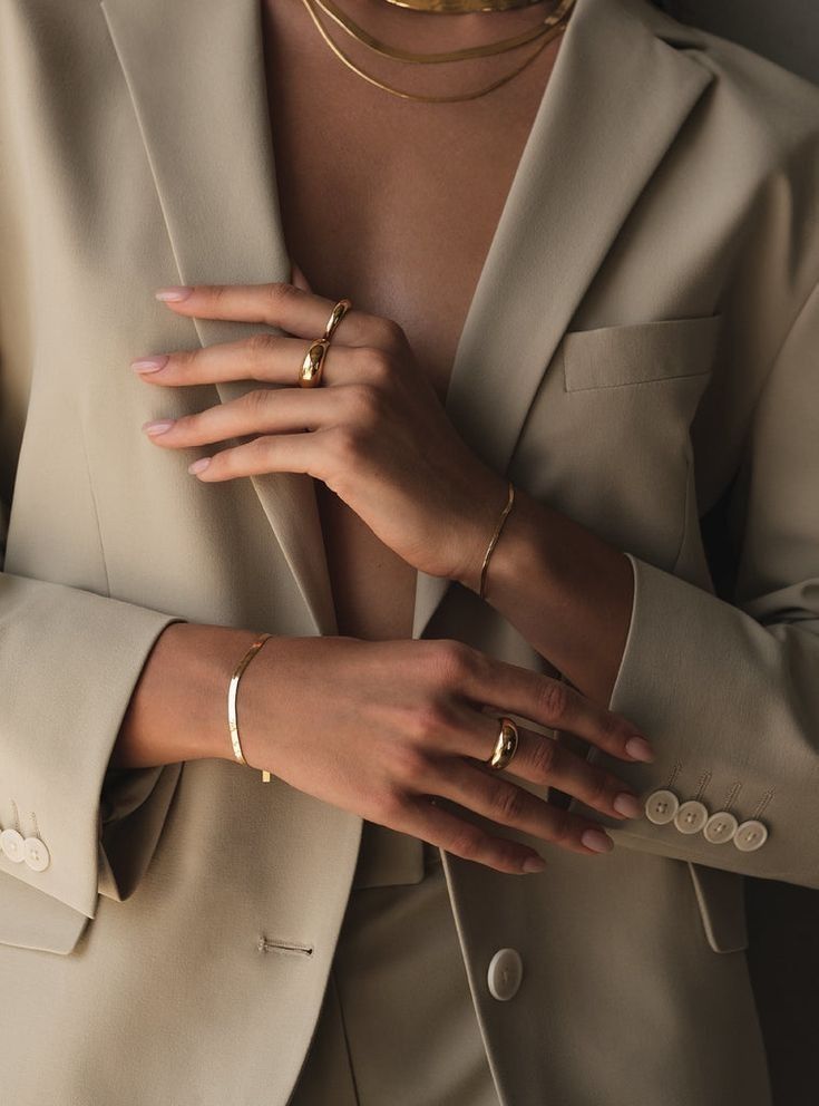 _ 39 Elegant woman in beige suit showcasing gold jewelry, including rings, bracelets, and necklace, against a sophisticated backdrop. | Sky Rye Design Elegant woman in beige suit showcasing gold jewelry, including rings, bracelets, and necklace, against a sophisticated backdrop.