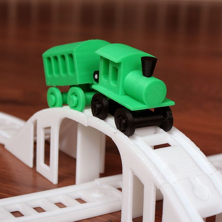 Green 3D-printed toy train on a white plastic track with a wooden background, showcasing creative use of 3D printing technology in toys.