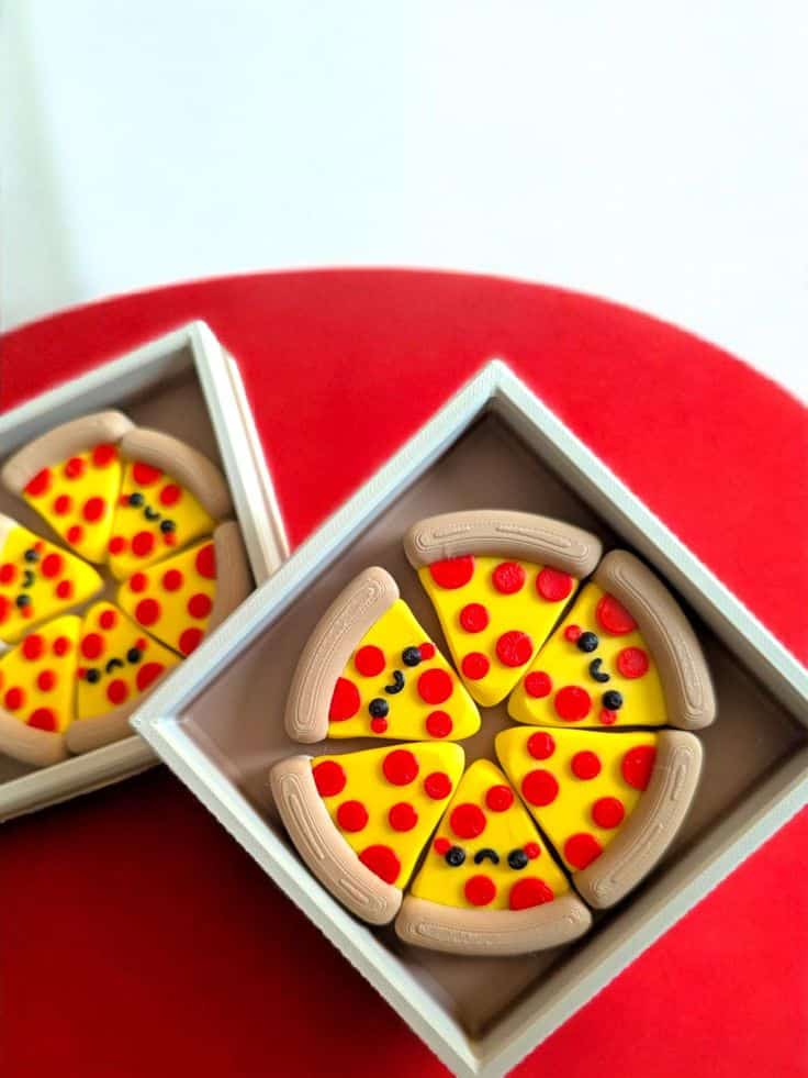 3D Printed Happy Pizzas Smiling mini pizza slice toys in a box on a red surface; colorful and playful decoration. | Sky Rye Design Smiling mini pizza slice toys in a box on a red surface; colorful and playful decoration.