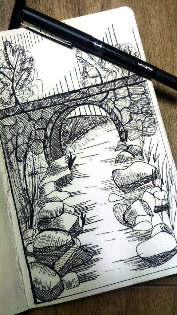 3c3c320e4b725007f2a67677082a0206 Ink sketch of a stone bridge over a river on a notebook, featuring rocks and trees, with a black pen laying on the page. | Sky Rye Design Ink sketch of a stone bridge over a river on a notebook, featuring rocks and trees, with a black pen laying on the page.