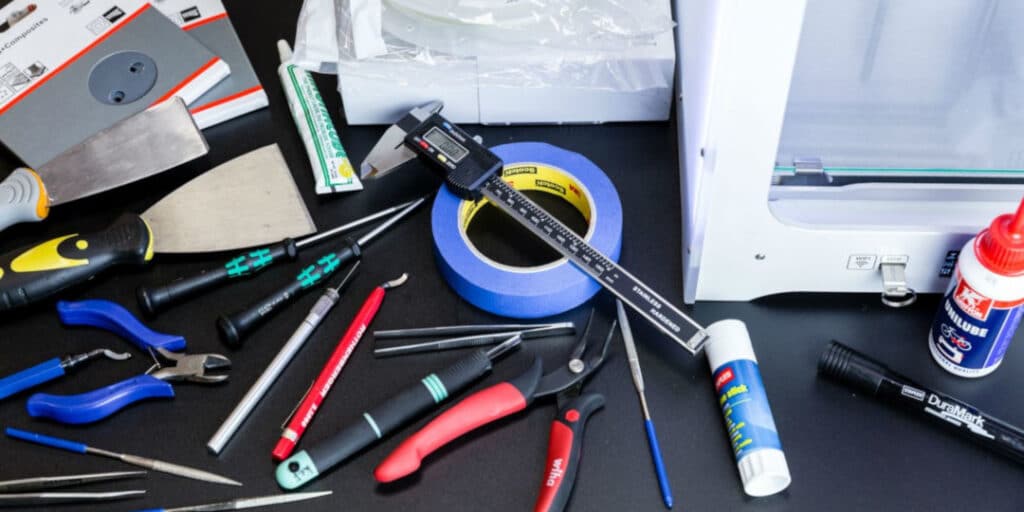 Various DIY tools on a black table: calipers, tape, scissors, glue, and screwdrivers. Ideal for crafting projects.