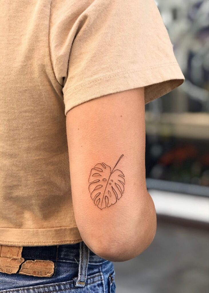 3f745da4493f882d9b70b313abc193d8 Simple monstera leaf tattoo on a person's arm, wearing a beige shirt and blue jeans. | Sky Rye Design Simple monstera leaf tattoo on a person's arm, wearing a beige shirt and blue jeans.
