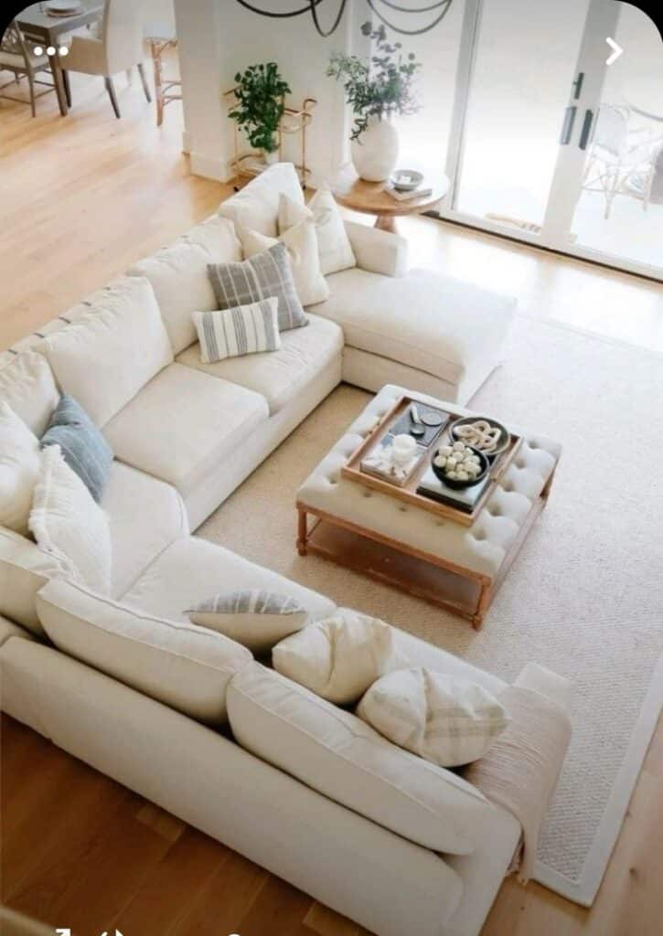 Stylish living room with a beige sectional sofa, cozy pillows, and a chic coffee table on a light rug.