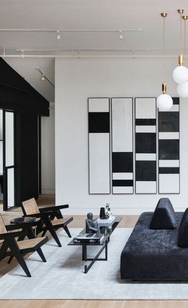 Modern living room with black and white abstract art, stylish black furniture, woven chairs, and pendant lights, featuring minimalist design.