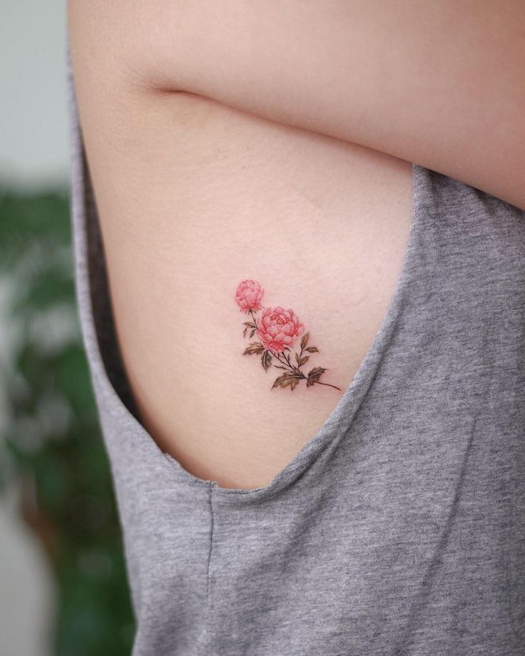 Minimalist pink rose tattoo on someone's side, beneath a gray tank top, highlighting delicate floral design and placement.
