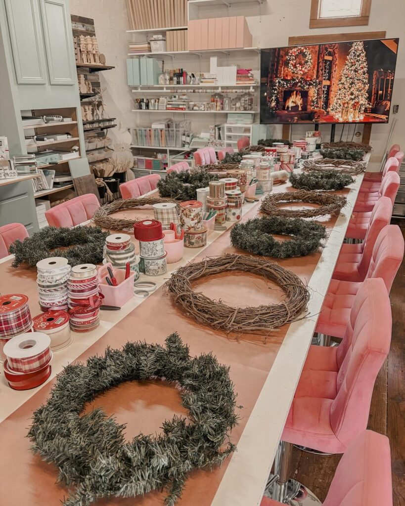 405afca8813126652d7343a8fac9beec Festive craft workshop with wreaths, ribbons, pink chairs, and a Christmas scene on a TV in the background. | Sky Rye Design Festive craft workshop with wreaths, ribbons, pink chairs, and a Christmas scene on a TV in the background.