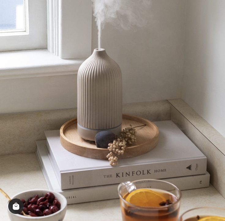 _ 44 Ceramic diffuser releasing steam on a wooden tray atop books, surrounded by tea and small snacks on a cozy windowsill. | Sky Rye Design Ceramic diffuser releasing steam on a wooden tray atop books, surrounded by tea and small snacks on a cozy windowsill.
