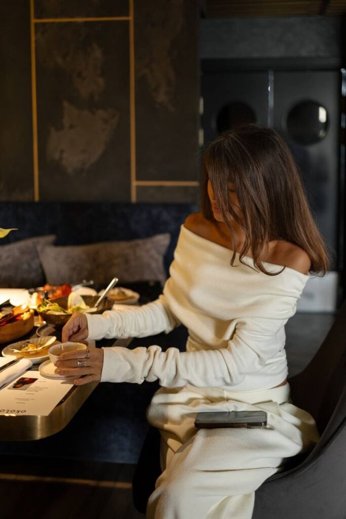 _ 46 Woman in a white dress enjoying coffee at a stylish restaurant table with various dishes, capturing a cozy and elegant dining moment. | Sky Rye Design Woman in a white dress enjoying coffee at a stylish restaurant table with various dishes, capturing a cozy and elegant dining moment.